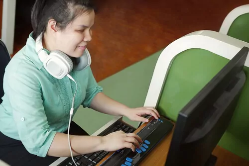 A blind woman looking at a computer screen with headphone around her neck.